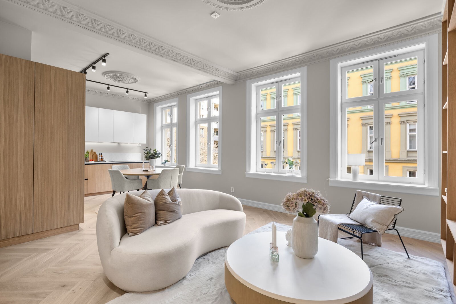 Lys stue med buet sofa, eikedetaljer og store vinduer
